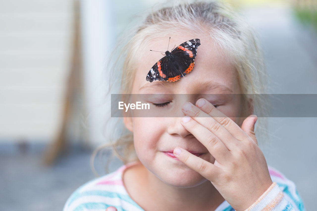 A beautiful black butterfly with orange spots, sits on a forehead of a caucasian girl of 7-8 years