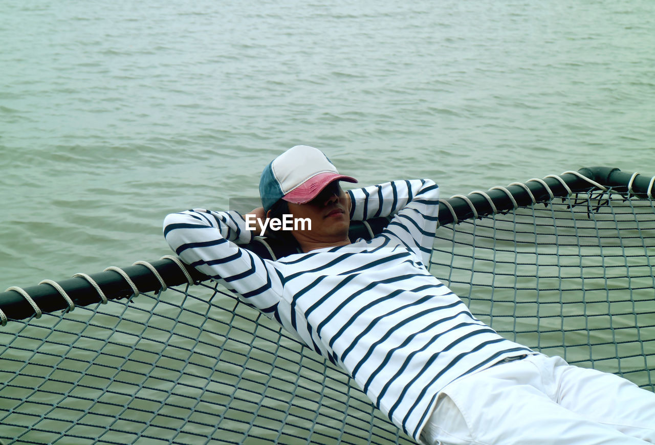 Young man relaxing on net over sea