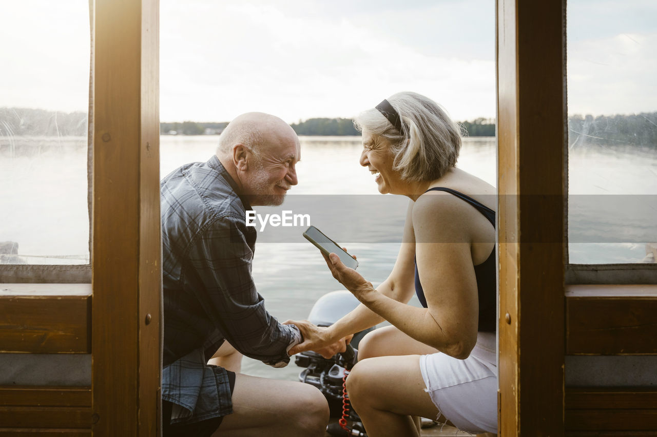 Happy senior couple with smart phone sitting on houseboat