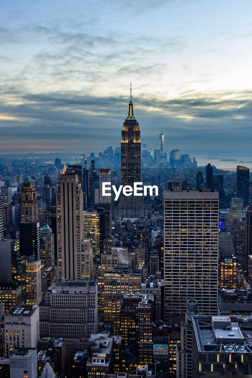 Empire state building amidst cityscape against sky at dusk