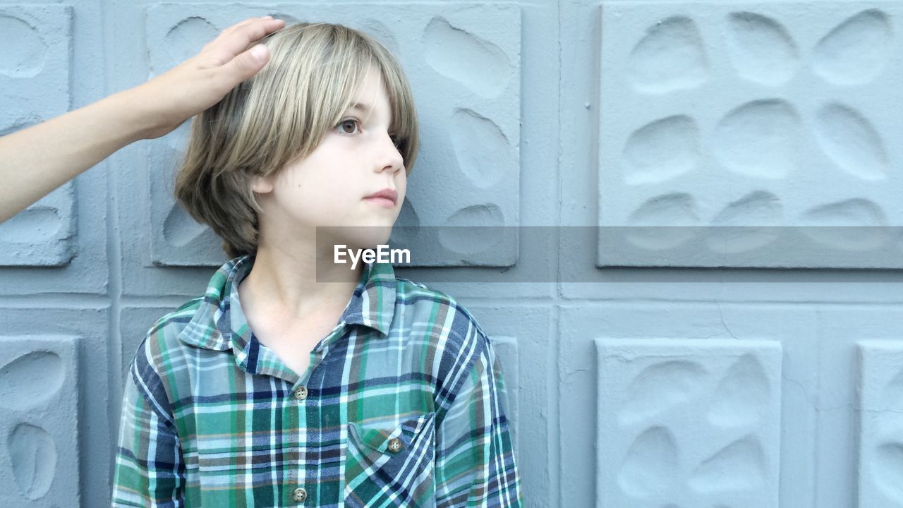 Cropped hand touching boy hair standing against patterned wall