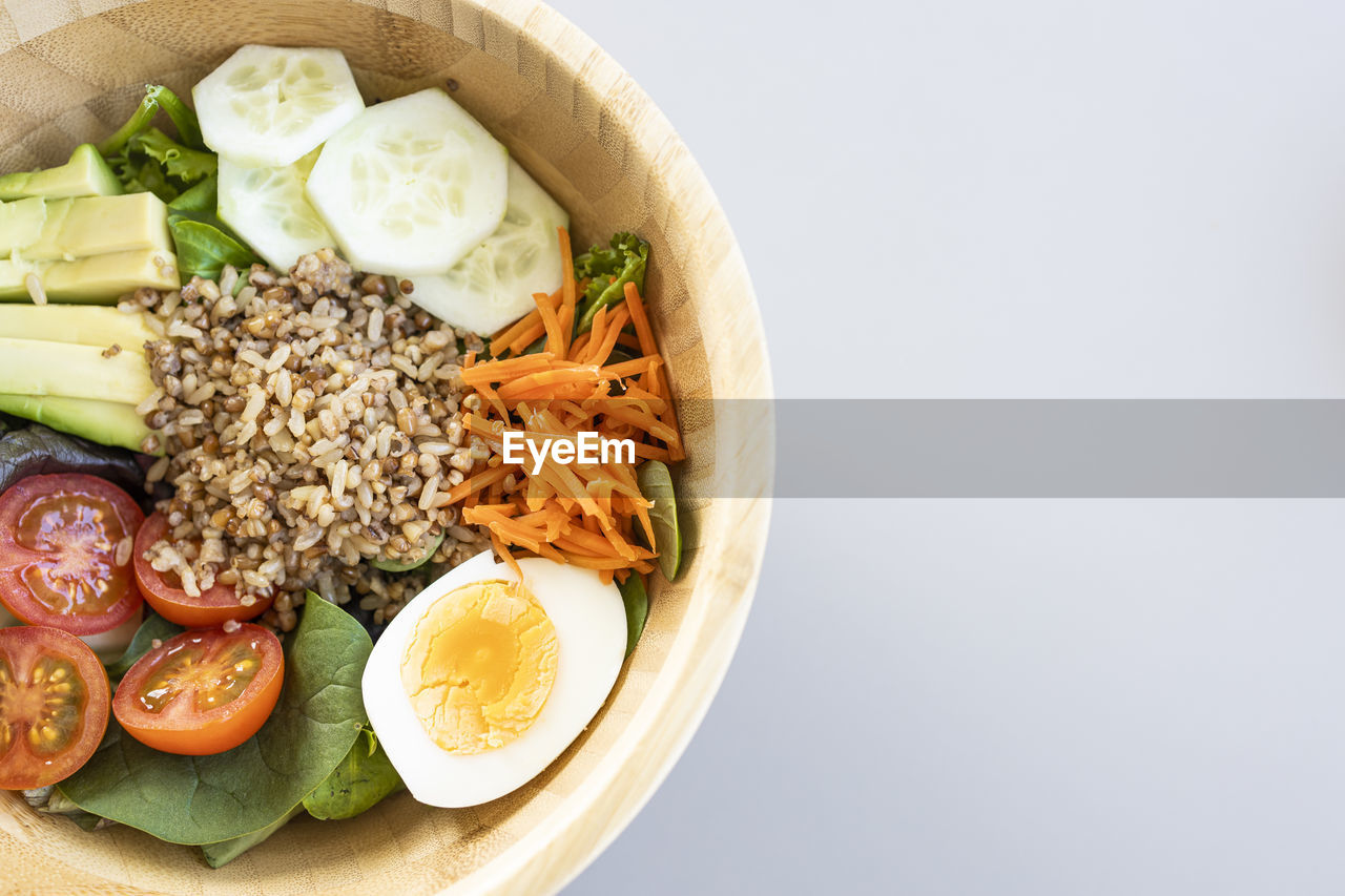 Brown rice salad with carrot, egg, cucumber, avocado, tomato and lamb's lettuce. top view.