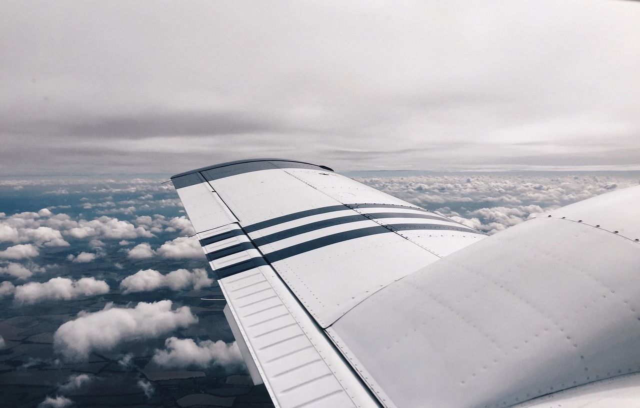 TILT IMAGE OF AIRPLANE FLYING OVER CLOUDS AGAINST SKY