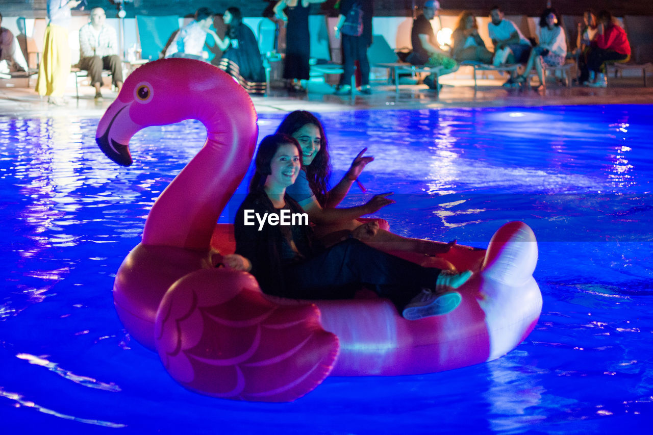 YOUNG WOMAN SITTING IN SWIMMING POOL AT WATER