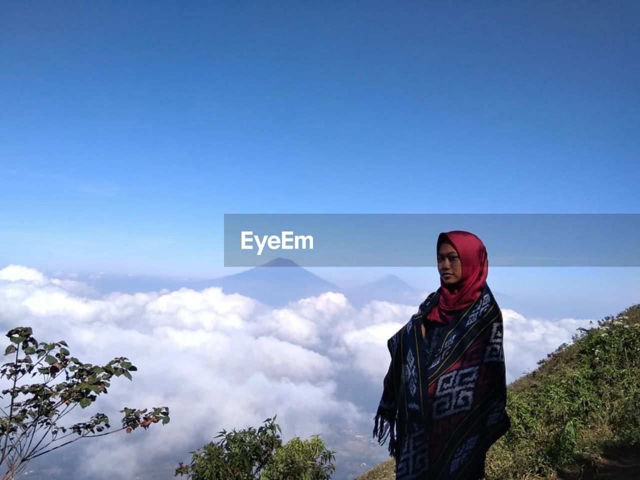 Woman wearing hijab standing on mountain against blue sky