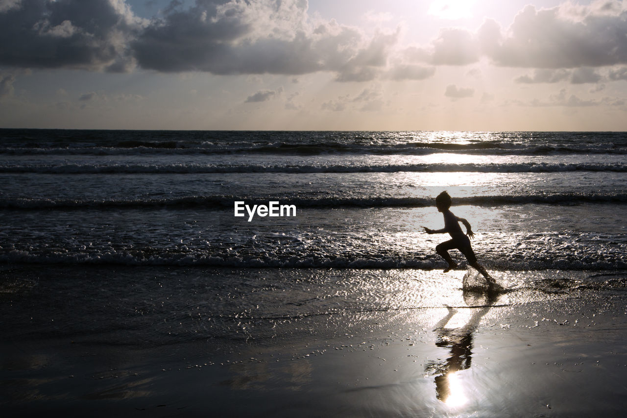 Boy running in sea against sky