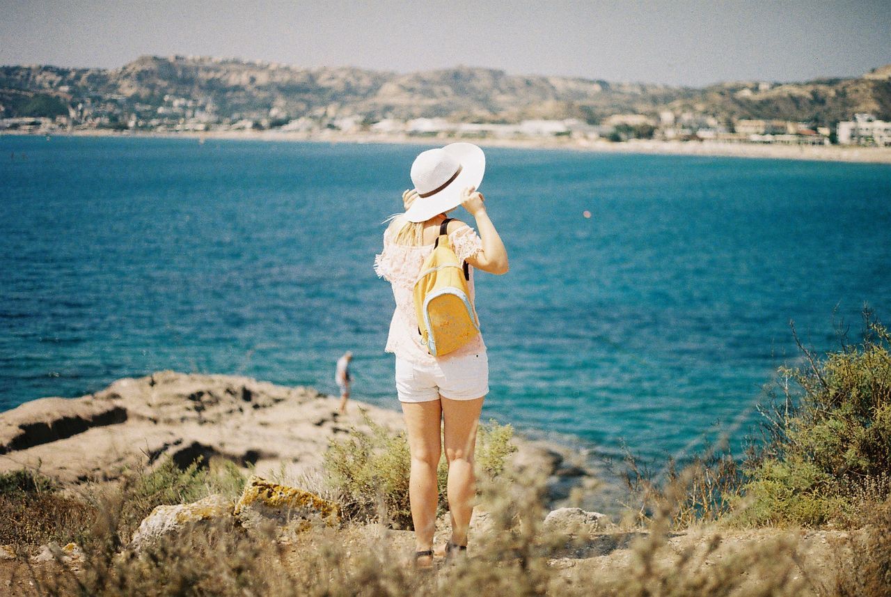 REAR VIEW OF WOMAN STANDING AT BEACH