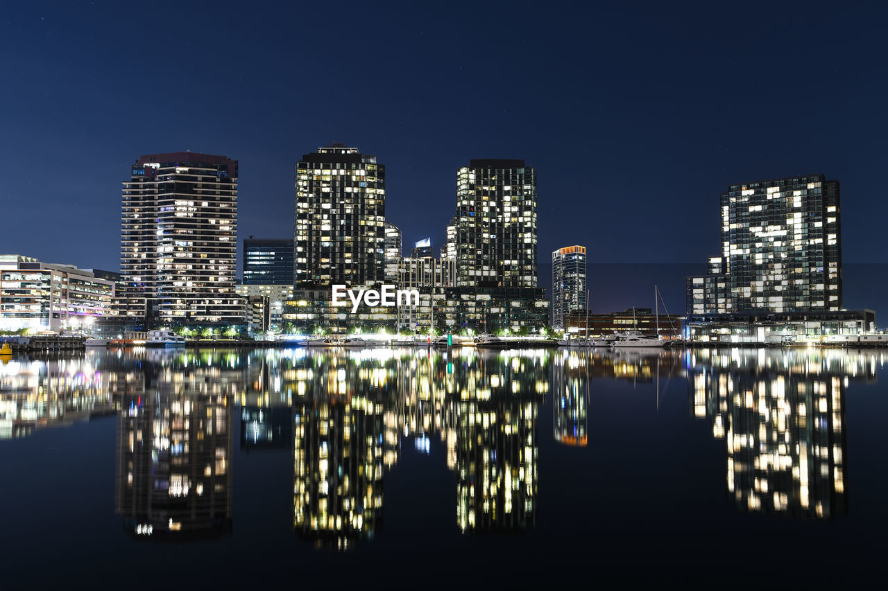 REFLECTION OF ILLUMINATED BUILDINGS IN LAKE AGAINST SKY