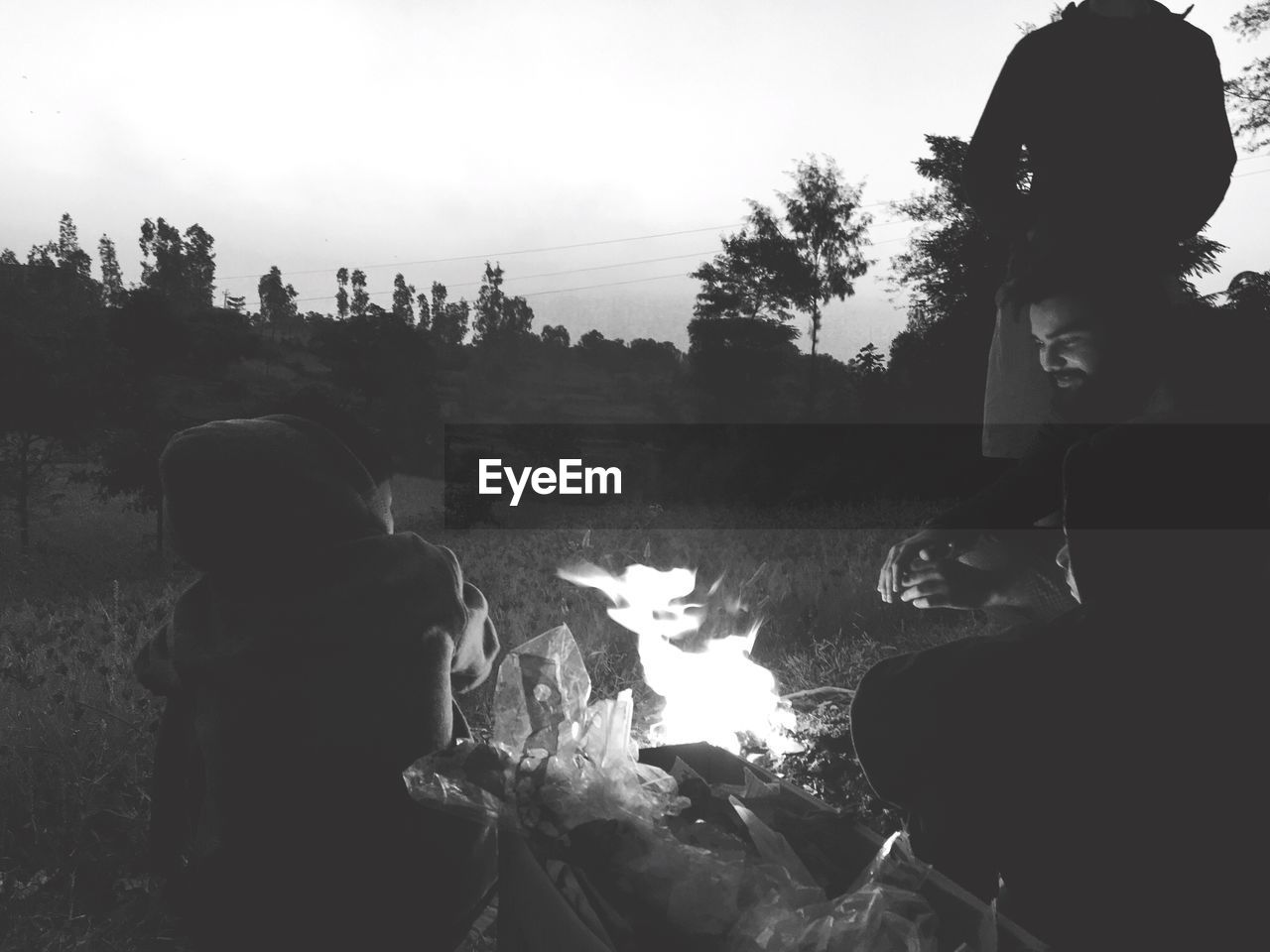 Friends sitting by campfire on field at dusk