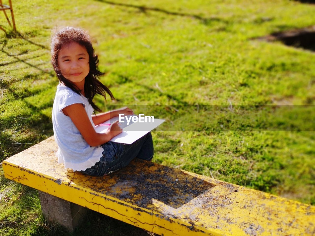 Portrait of girl with book sitting on bench in park