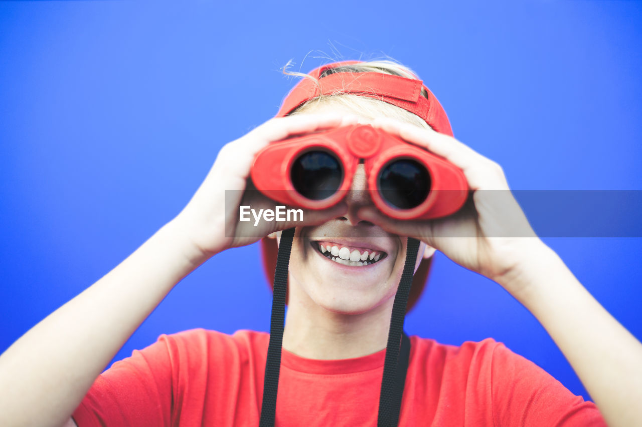 Portrait of smiling boy looking through binoculars against blue background