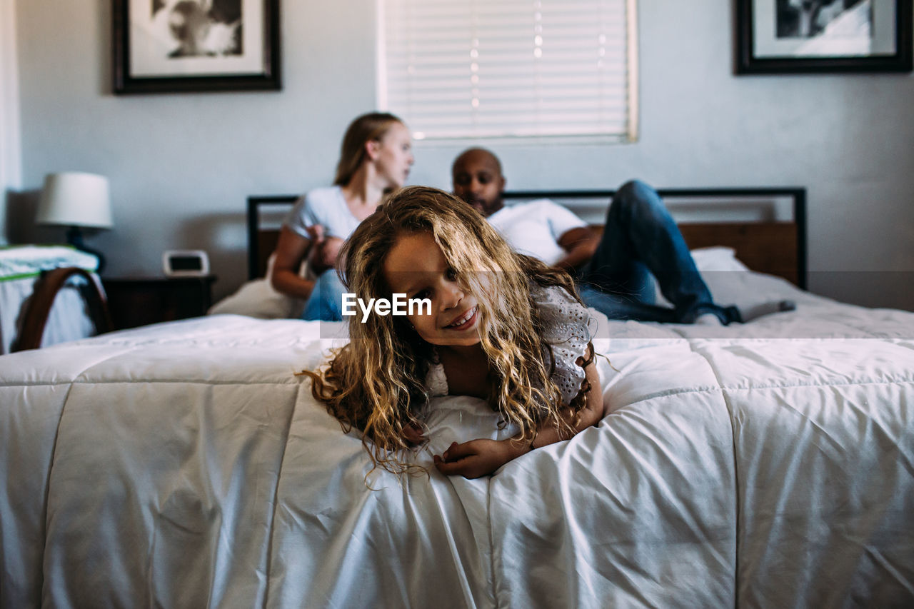 Young girl playing on the end of the bed with parents in background