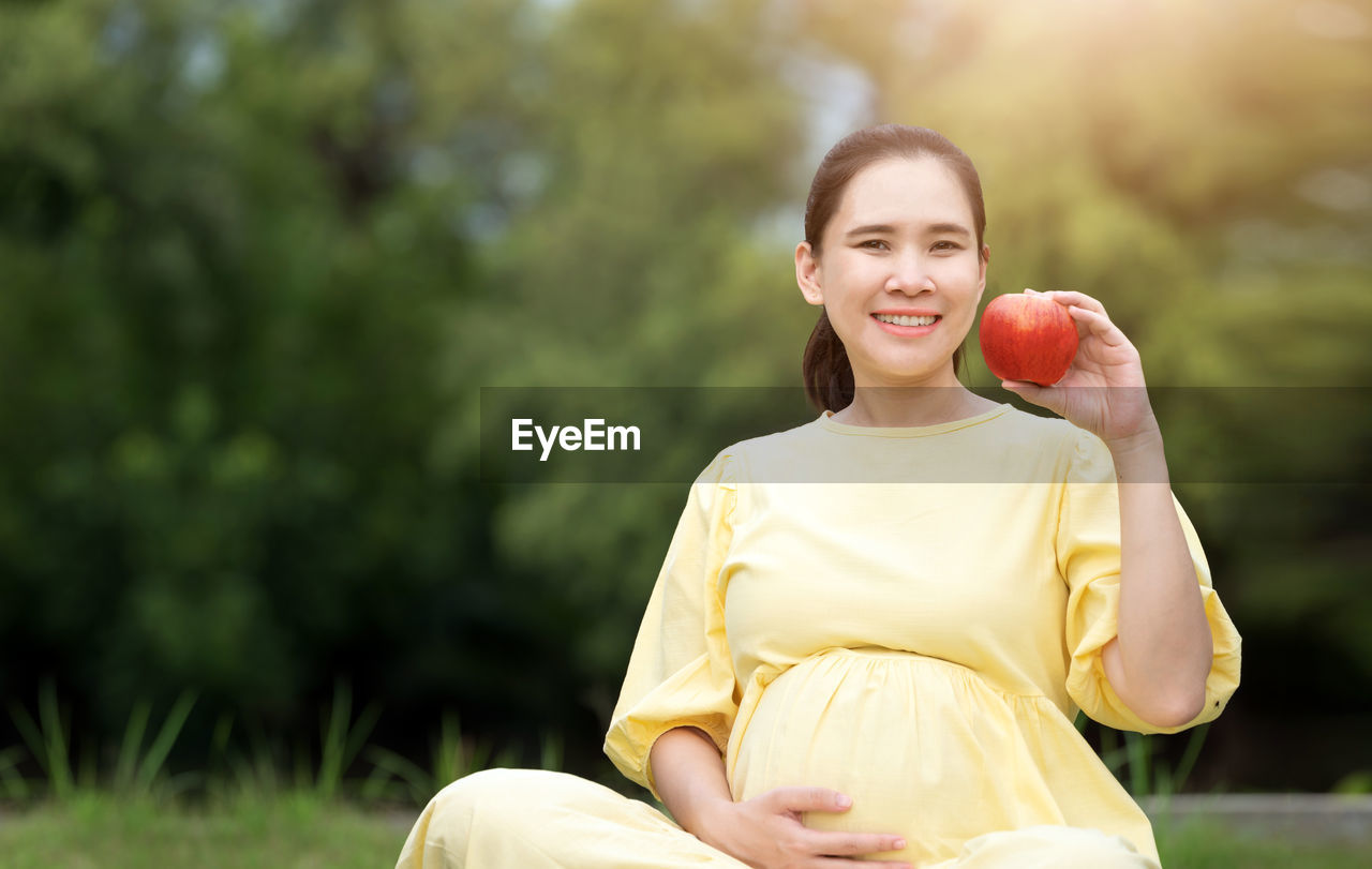 PORTRAIT OF SMILING WOMAN HOLDING PLANT OUTDOORS