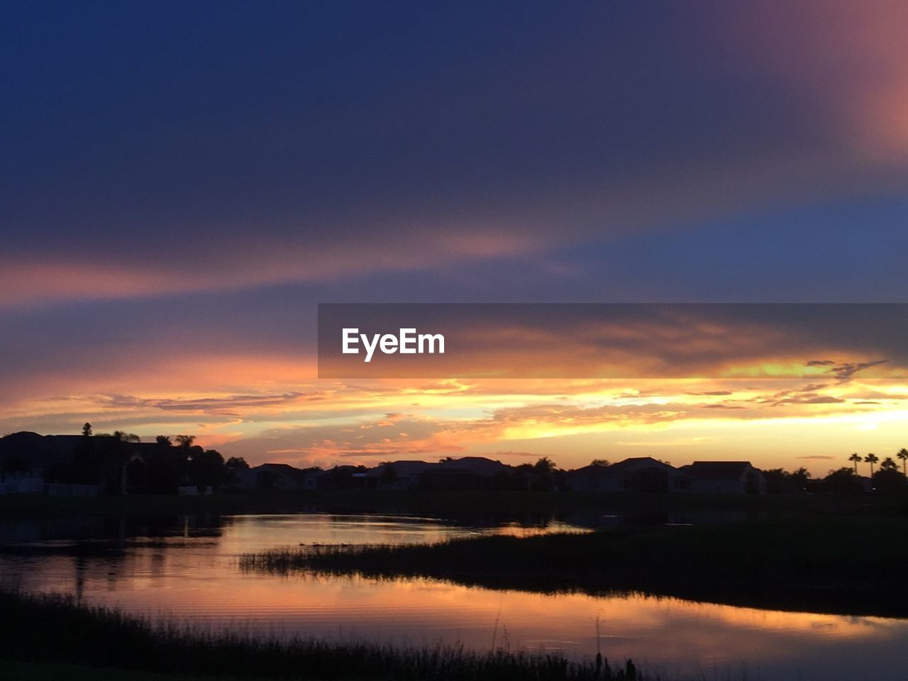 Scenic view of river against cloudy sky at sunset