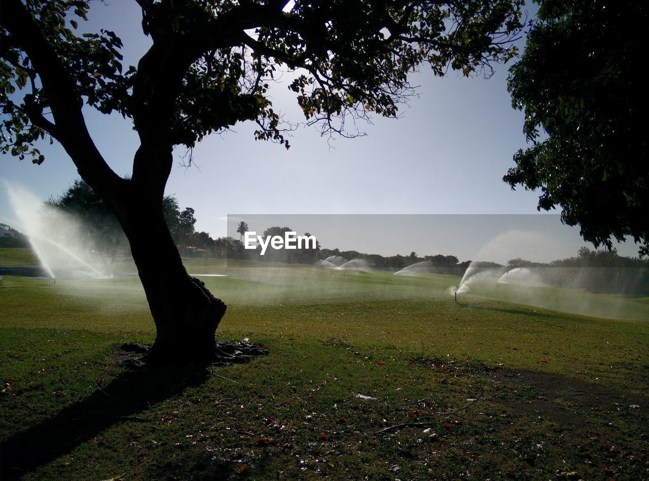 Irrigation sprinkler on golf course against sky on sunny day