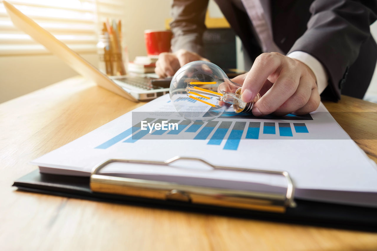 Midsection of businessman holding light bulb on paperwork