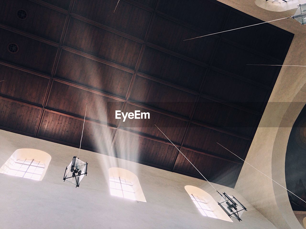 Low angle view of lighting equipment hanging from wooden ceiling in church