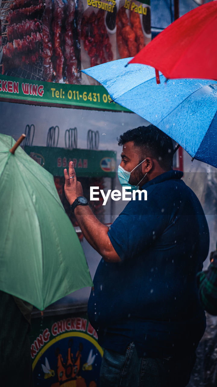 MIDSECTION OF MAN HOLDING UMBRELLA STANDING AT RAIN