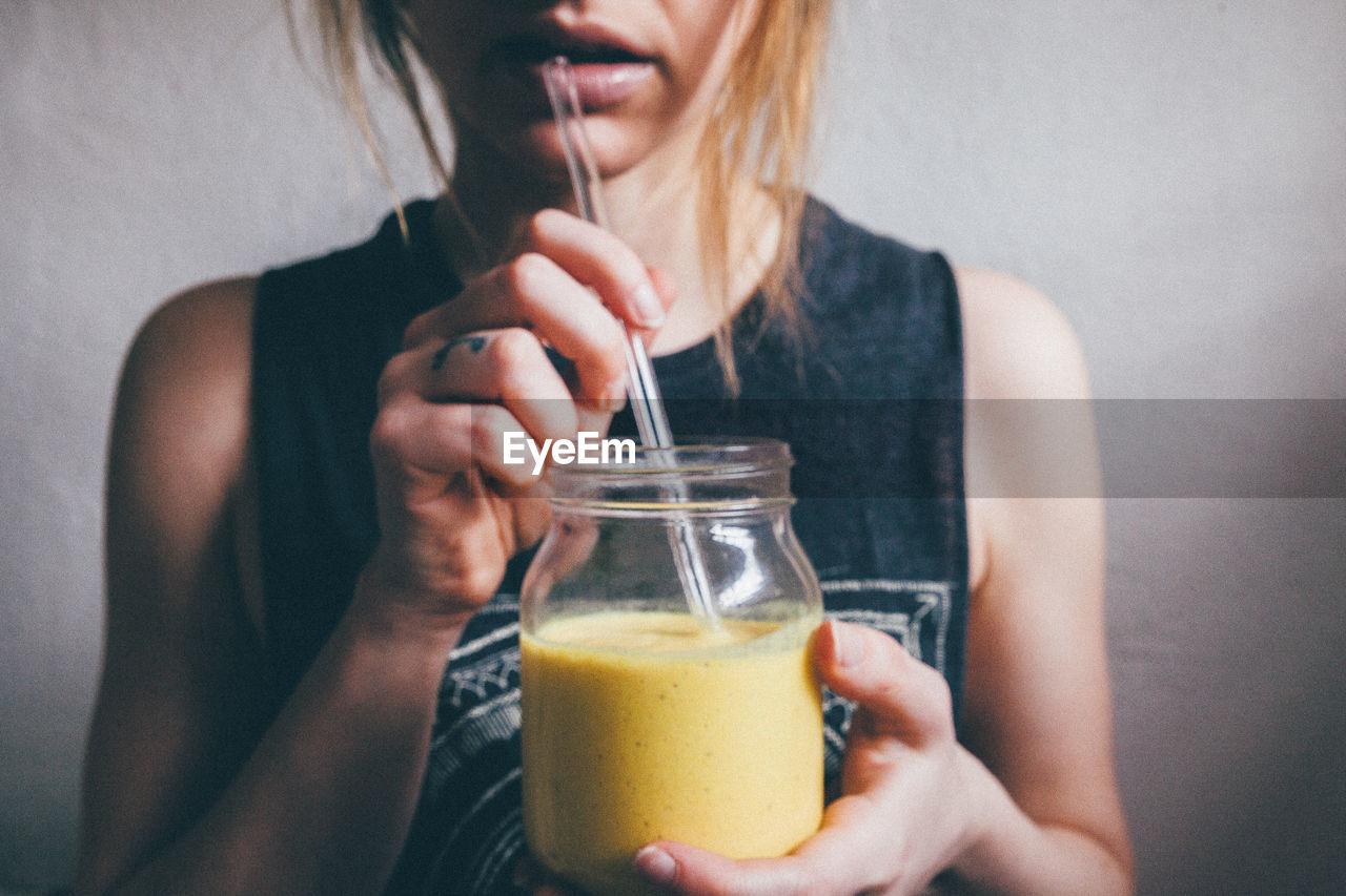 Midsection of woman drinking smoothie against wall