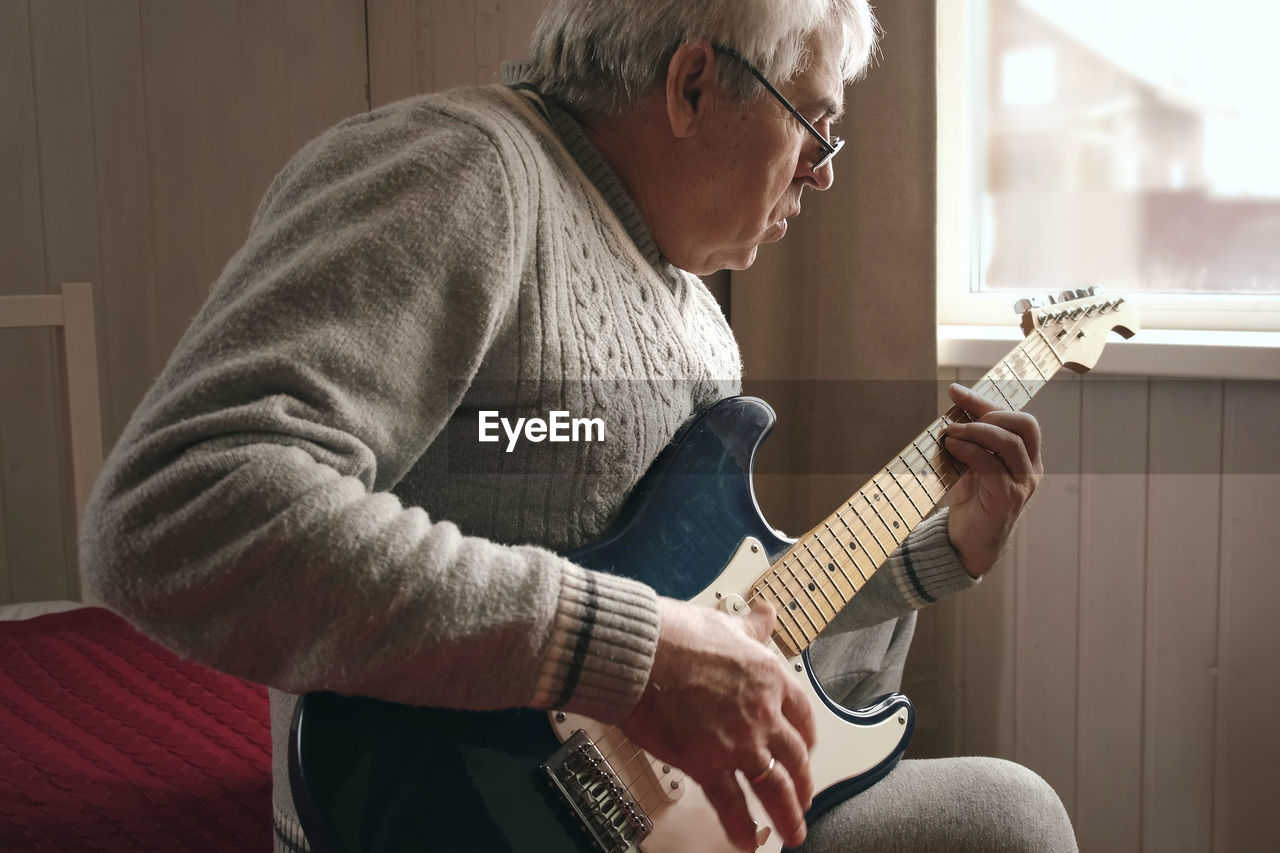 Senior man is playing guitar. elderly man sitting on the sofa and playing guitar. portrait of a gray