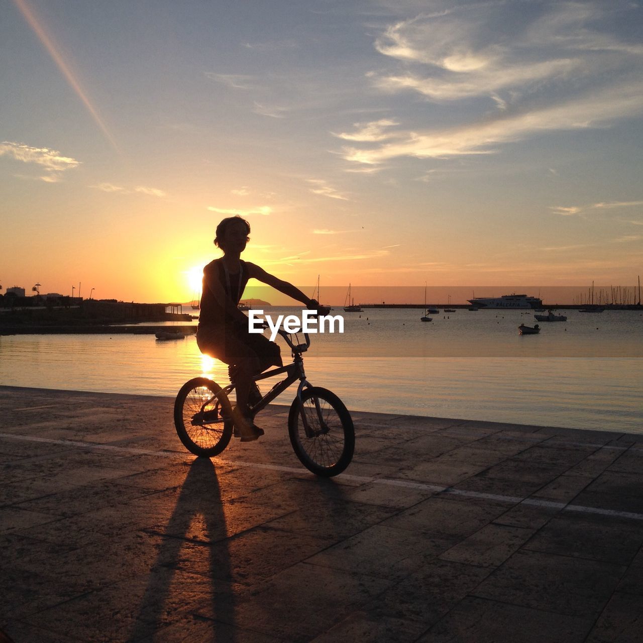 Silhouette boy riding bicycle at beach against sky during sunset