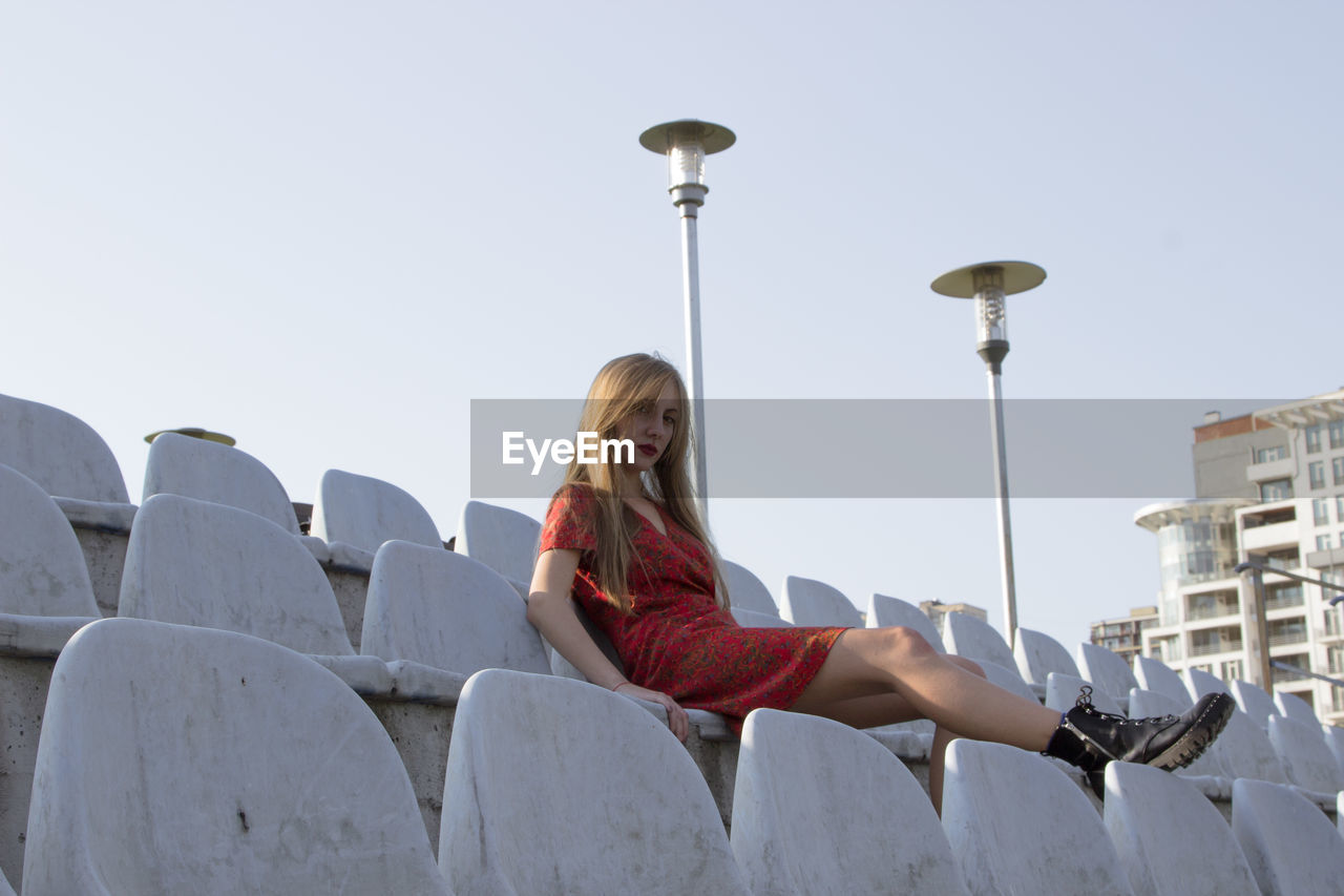 Portrait of young woman sitting at stadium against clear sky