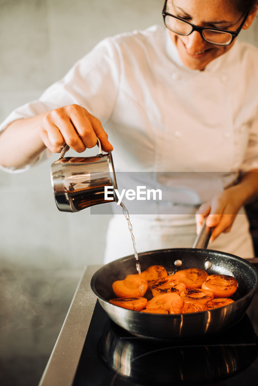 Female chef is adding water to cooking apricots