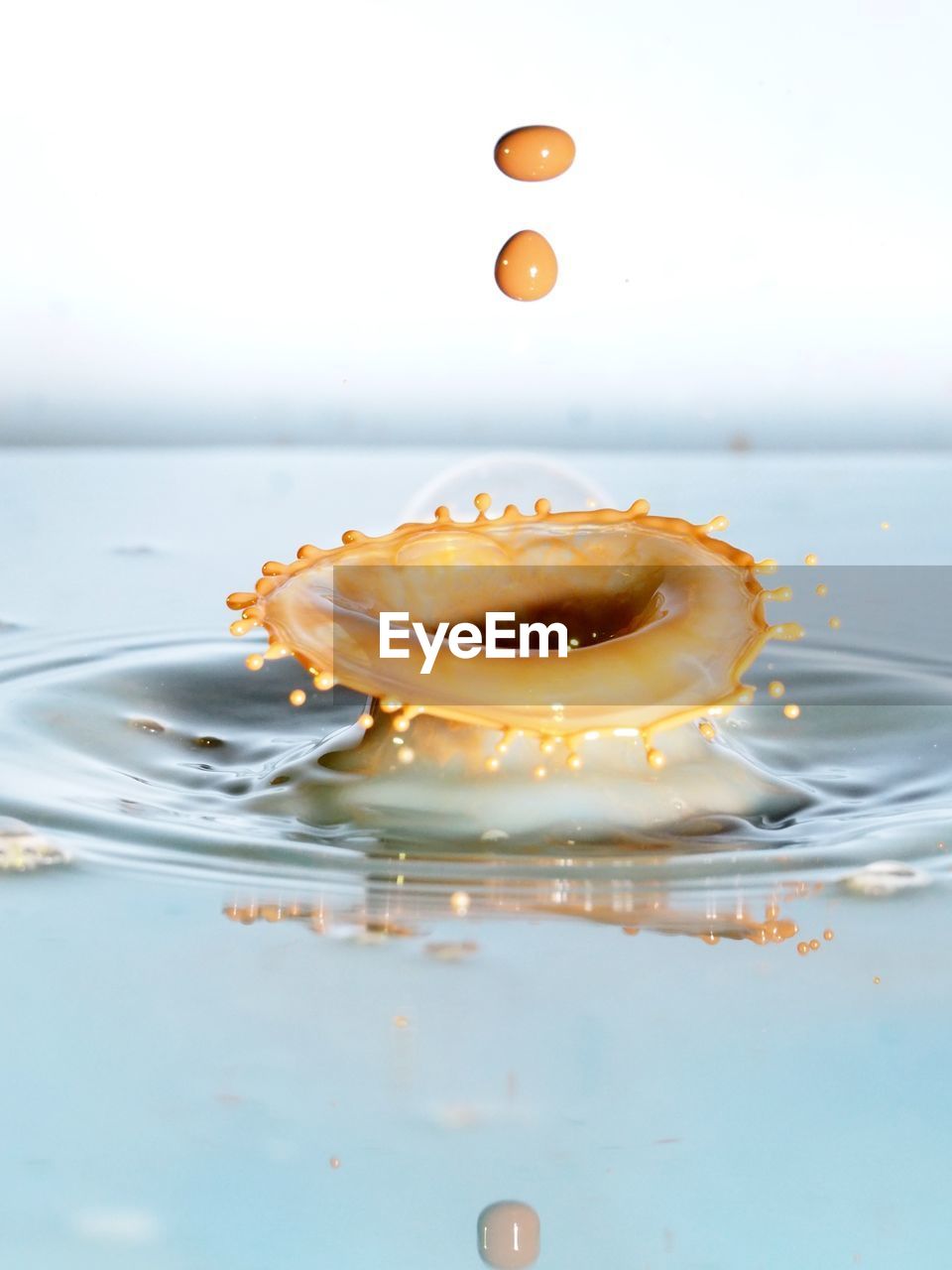 Close-up of water drop splashing on milk against white background