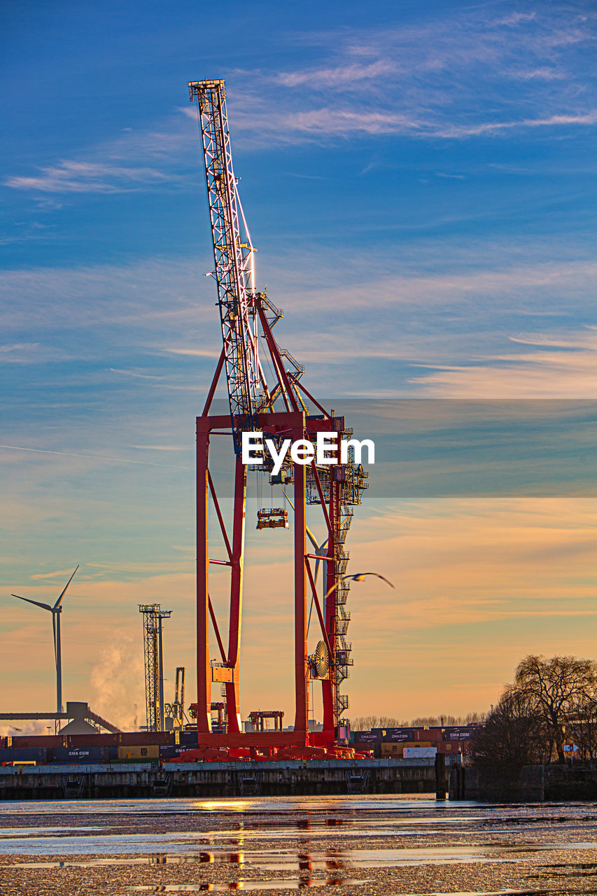 Ferris wheel by river against sky during sunset