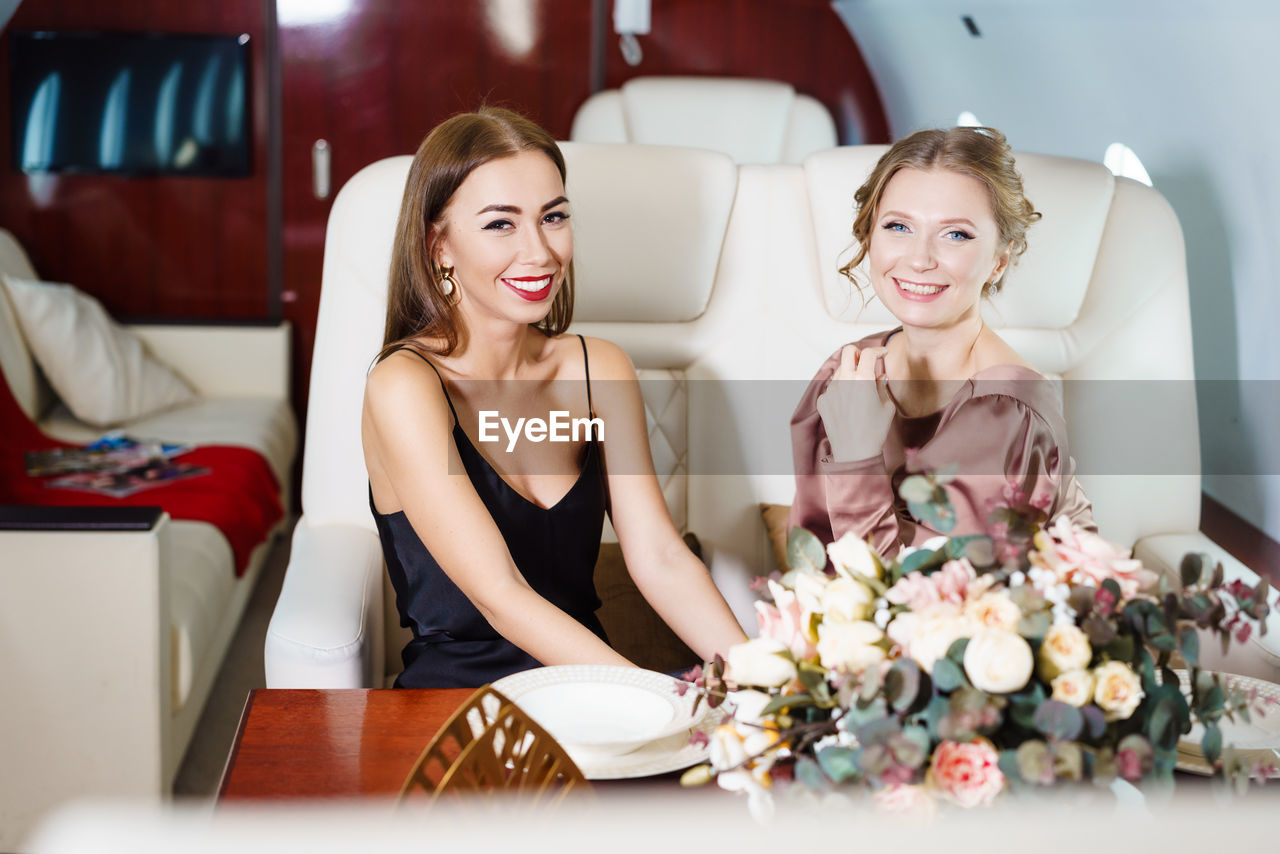 Two beautiful stylish women are sitting at table in private jet. celebrating
