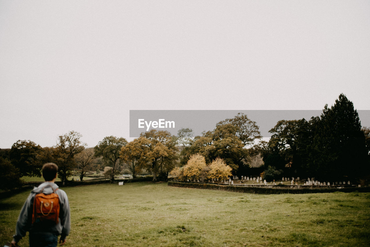 Rear view of man walking on field against clear sky