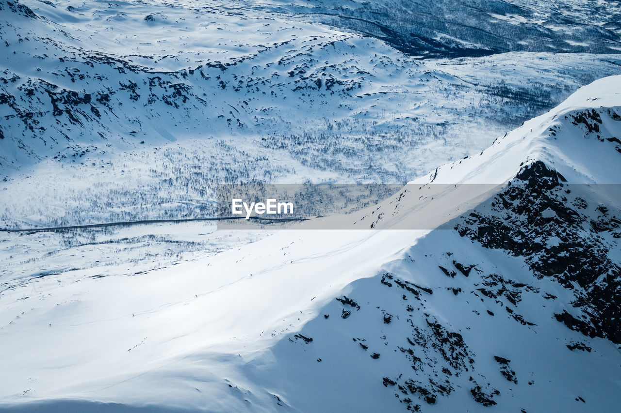 High angle view of snow covered mountain outside narvik with skiers on it