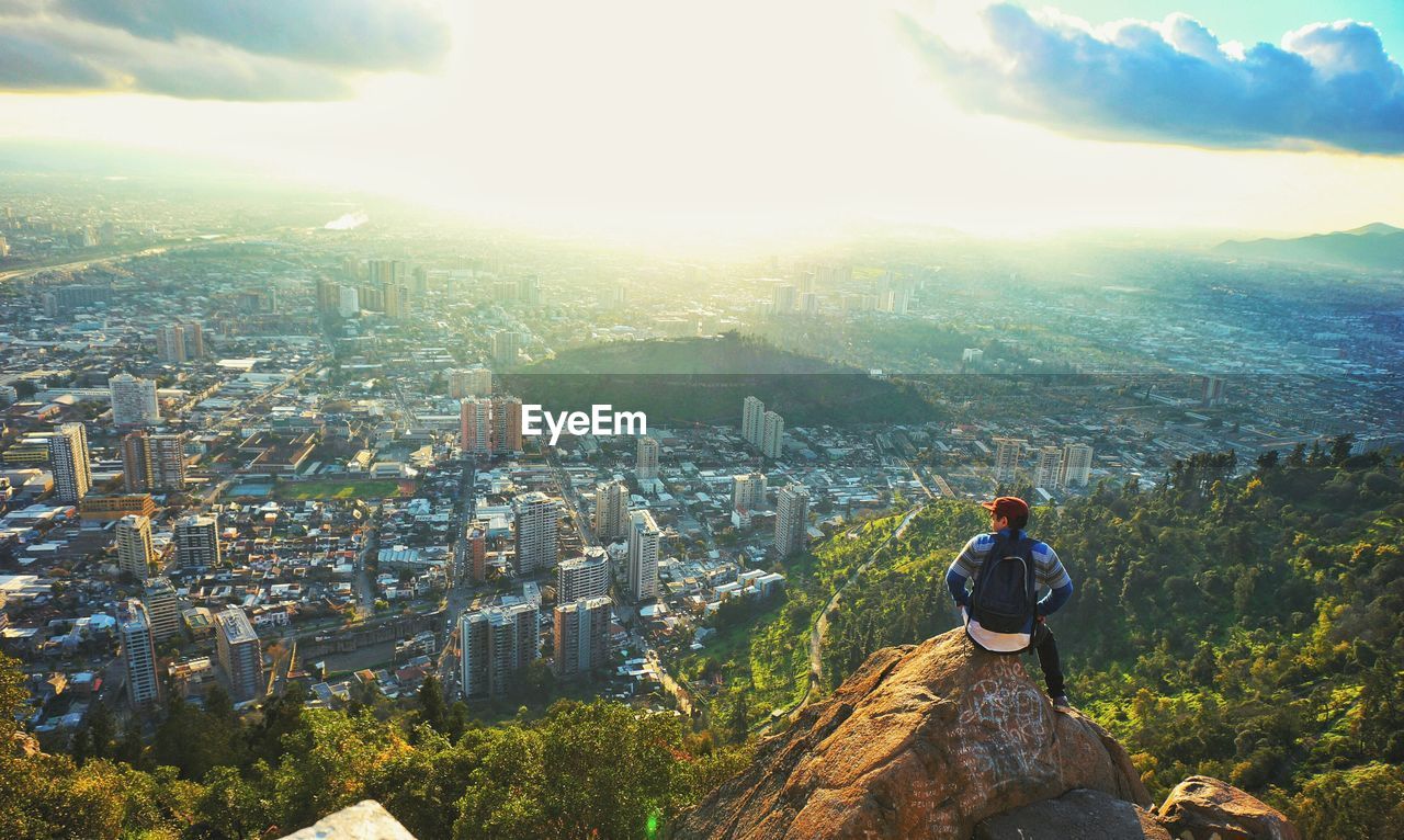 Rear view of man sitting on mountain against cityscape