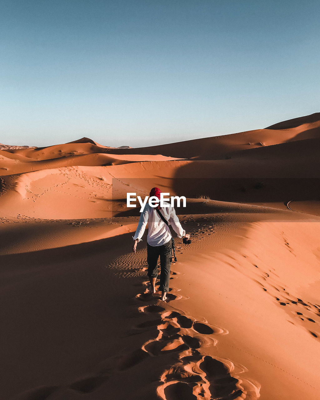 Rear view of man walking on sand dune in desert against clear sky