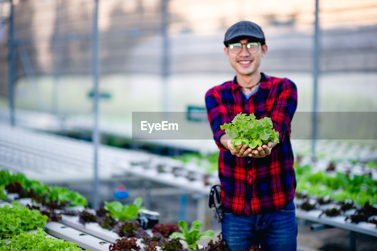 PORTRAIT OF SMILING YOUNG MAN STANDING ON PLANT