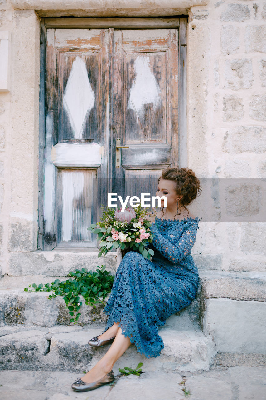 Full length of bride holding flower bouquet sitting by door