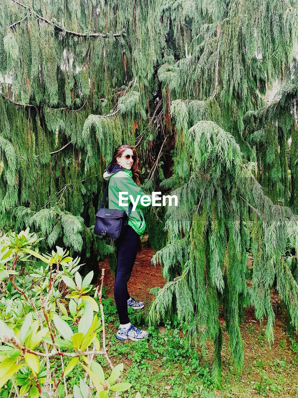 Side view of woman standing by tree at field