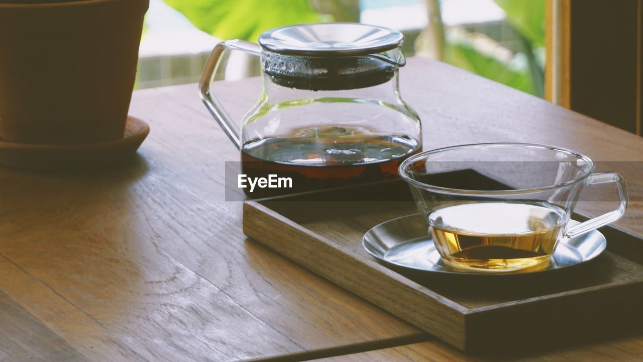 Close-up of glass tea pot and mug served on wooden table