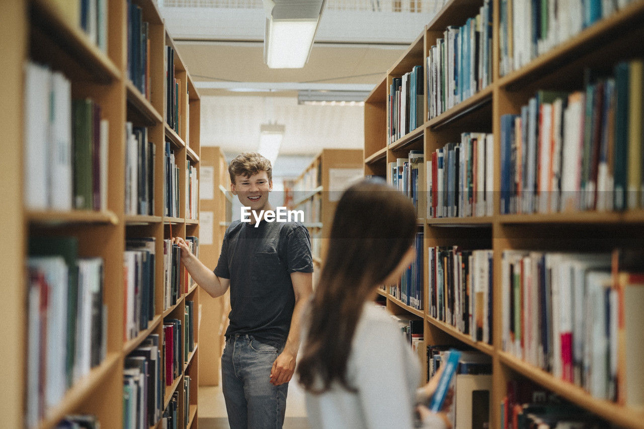 Happy students searching books on bookshelf in library at university