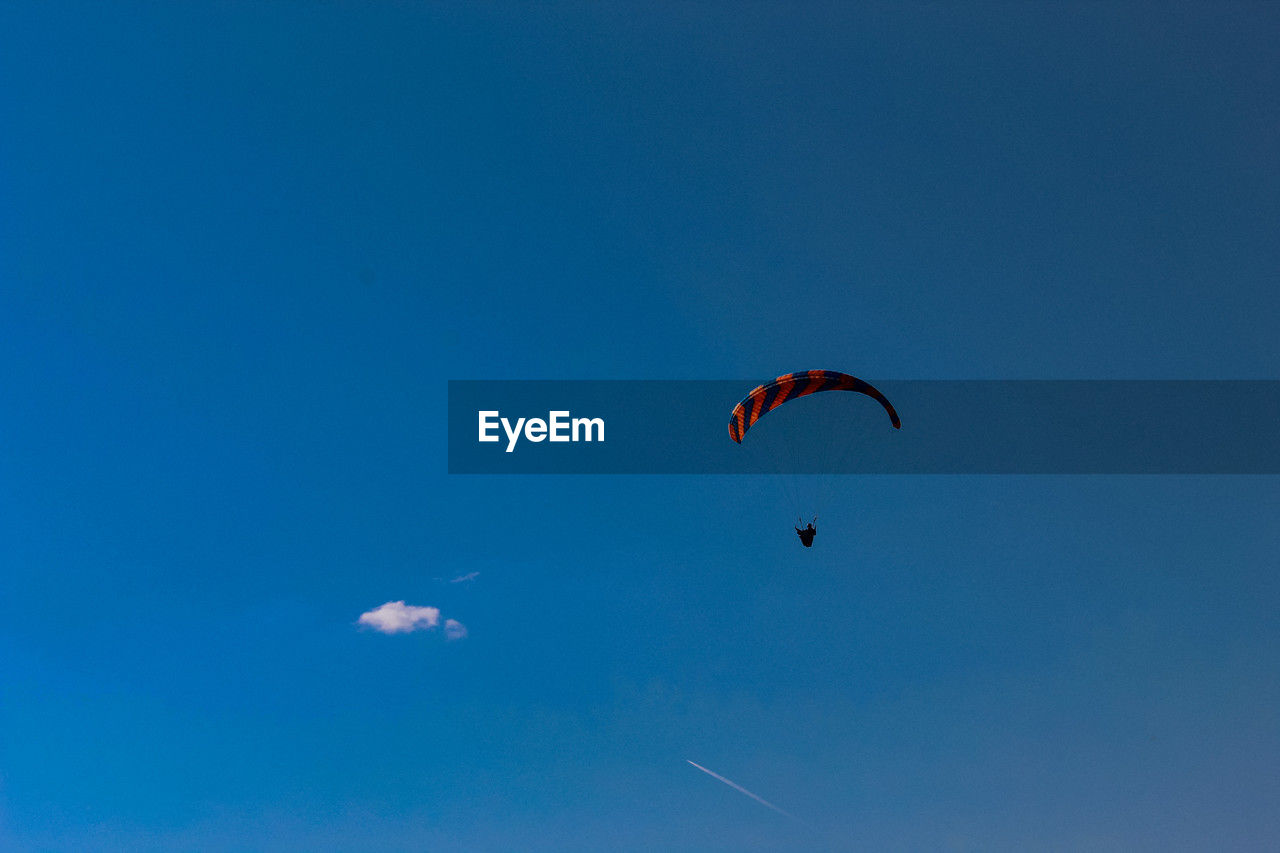 low angle view of man paragliding against clear blue sky