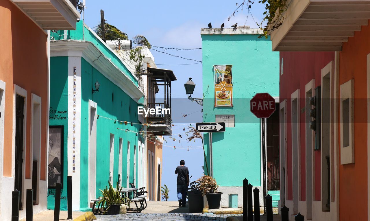 Rear view of man walking on footpath amidst houses