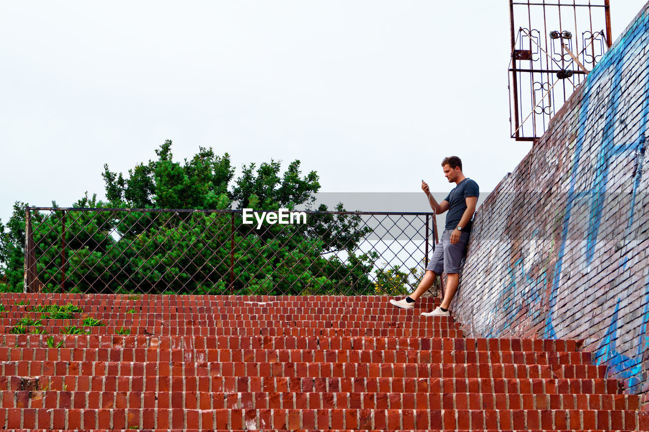 Man standing on steps by trees against sky