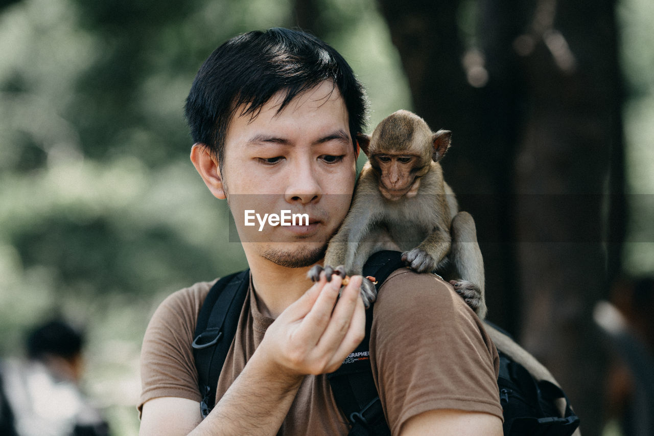 Monkey taking food from man while sitting on his shoulder