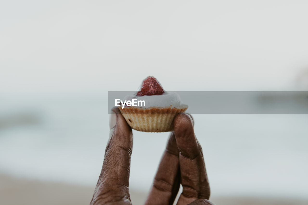Close-up of hand holding a cup cake against sky