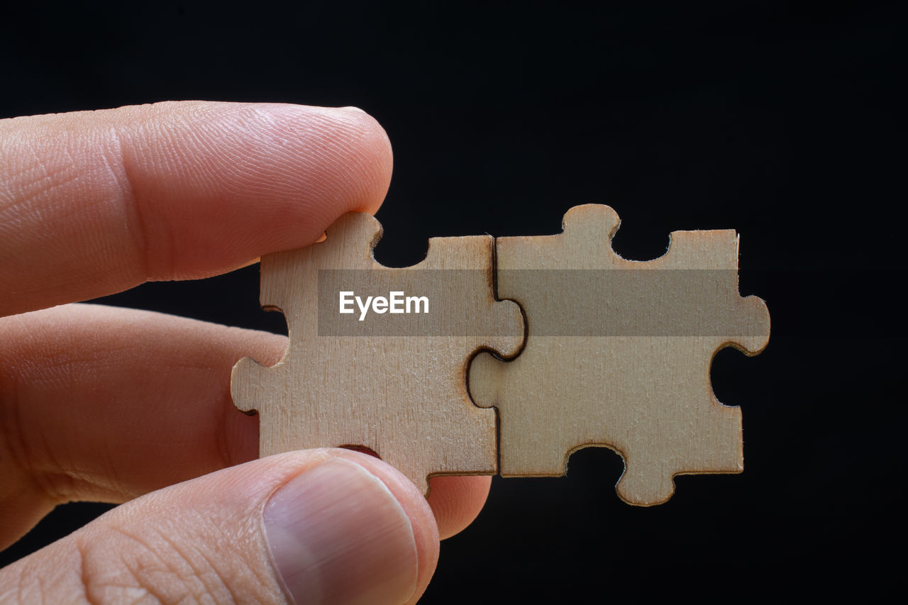 Close-up of hand holding jigsaw pieces against black background