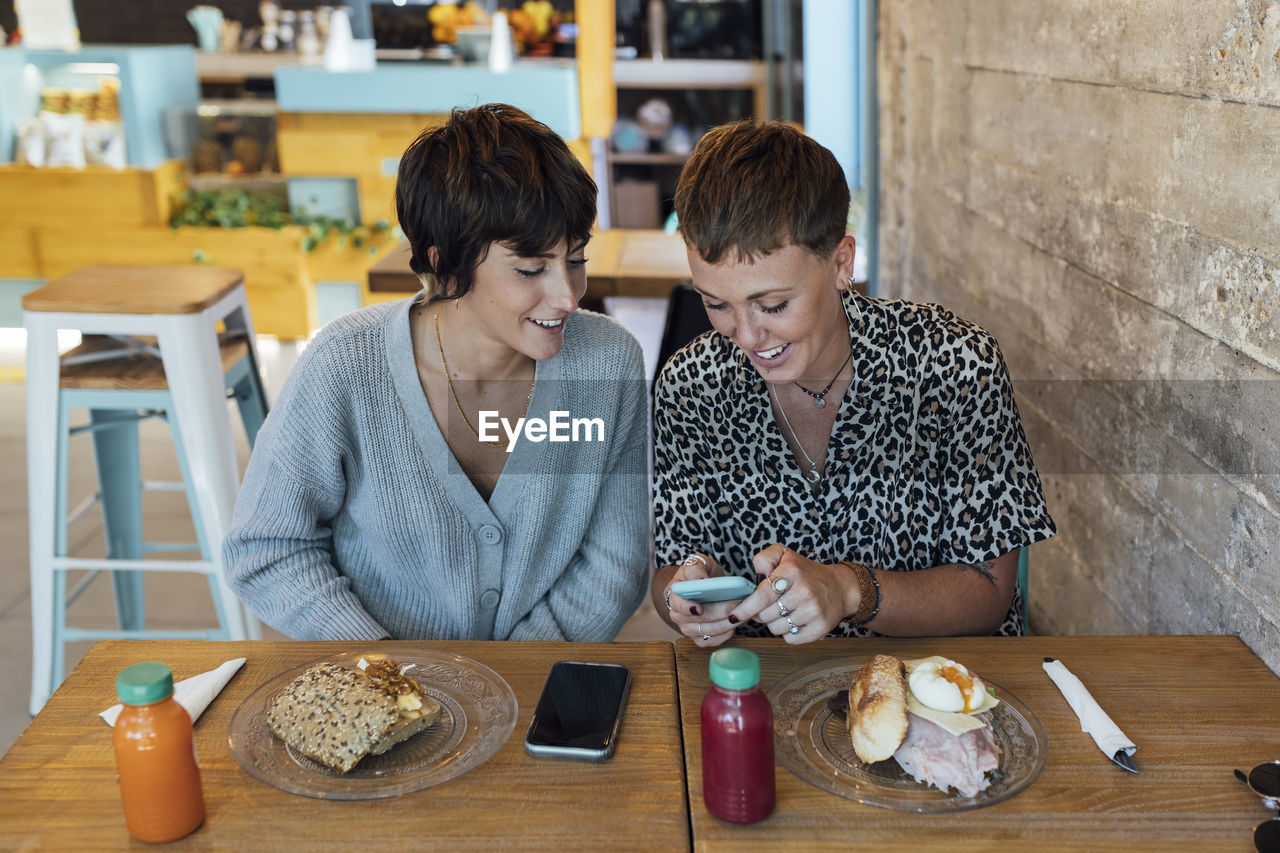 Woman using mobile phone while sitting by friend at restaurant