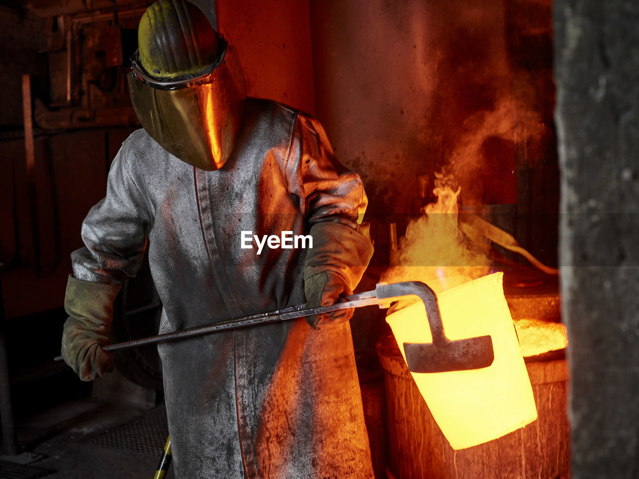 Foundry worker carrying burning container with hand tool in industry