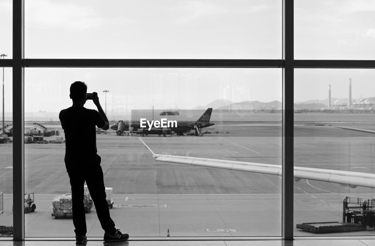 Rear view of silhouette man photographing against window at airport