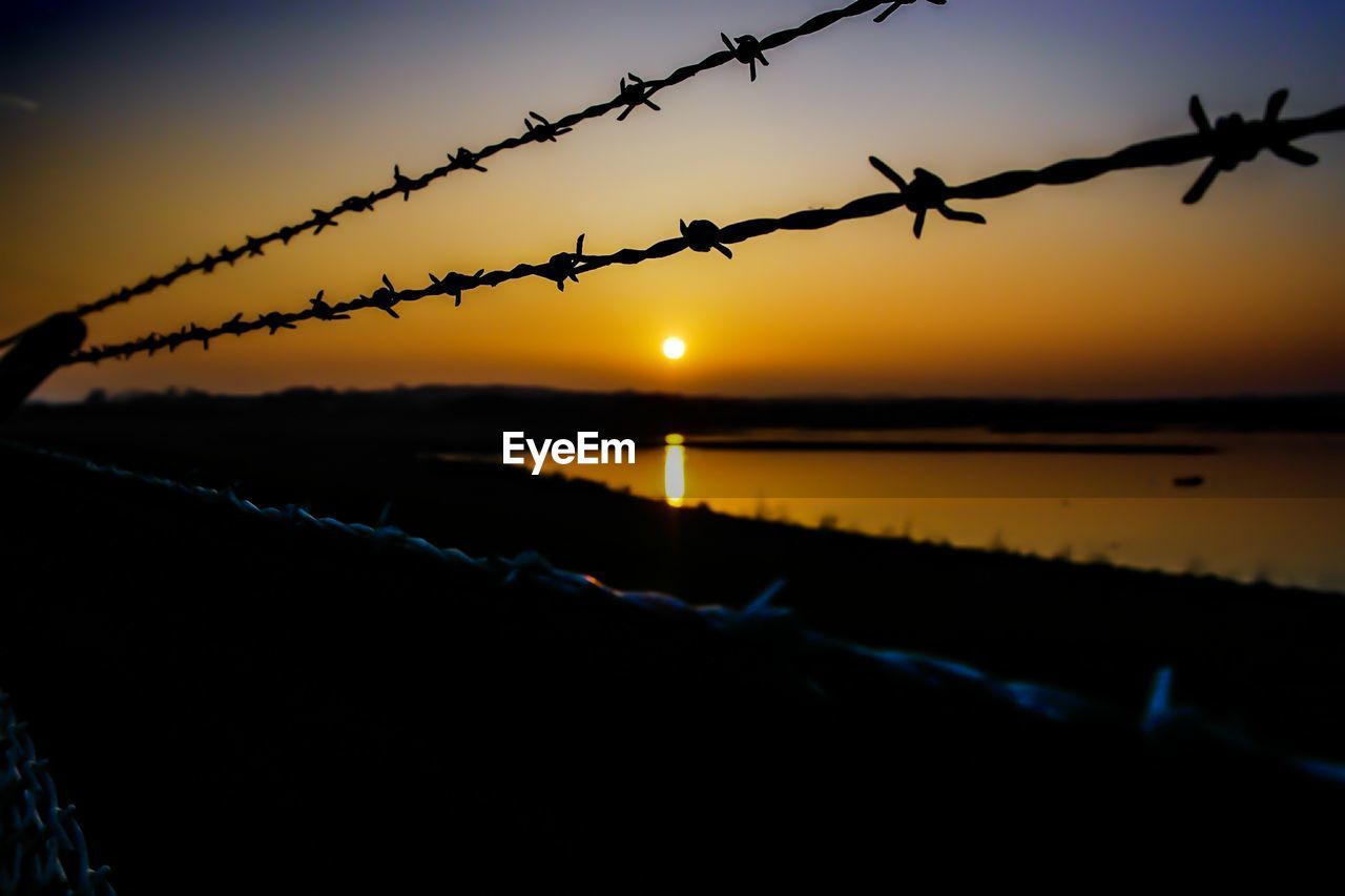 Barbed wire on lakeshore during sunset