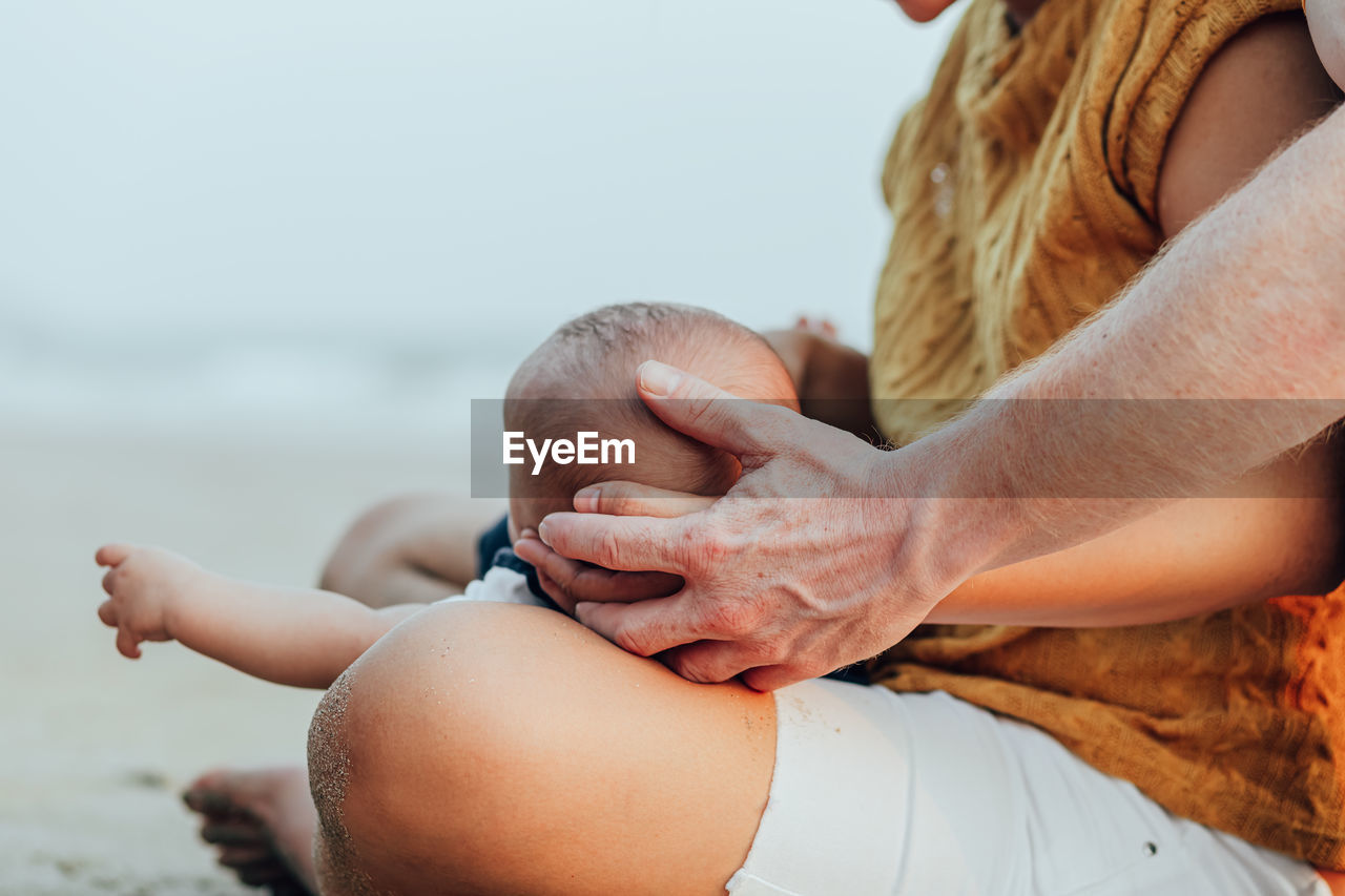 Cropped image of father touching hand of mother while holding baby outdoors